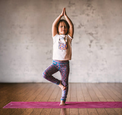 Child in tree pose on pink yoga mat
