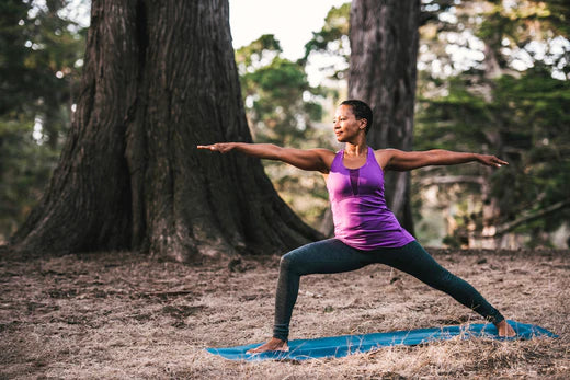 woman does warrior 2 pose in the forest for earth day