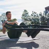 Person seated on a Yoga Mat in Boat Pose with the Conditioning Rope in each hand