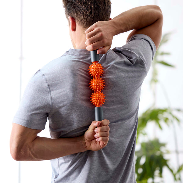 Person standing showing the upper back with the Restore Pressure Point Massager between the shoulder blades being held with both hands