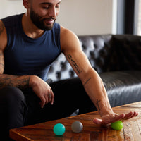 Person using the Gaiam Restore Hand Therapy Kit - hand on lime ball rolling it across table