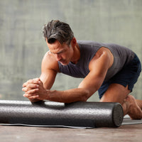 Person using the Essentials High-Density Foam Roller to massage the arms while kneeling on the ground 