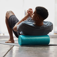 Person using the Essentials High-Density Foam Roller  to massage the upper back while on the ground 