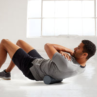 Person on ground with Restore Compact Textured Foam Roller under lower back to help massage 