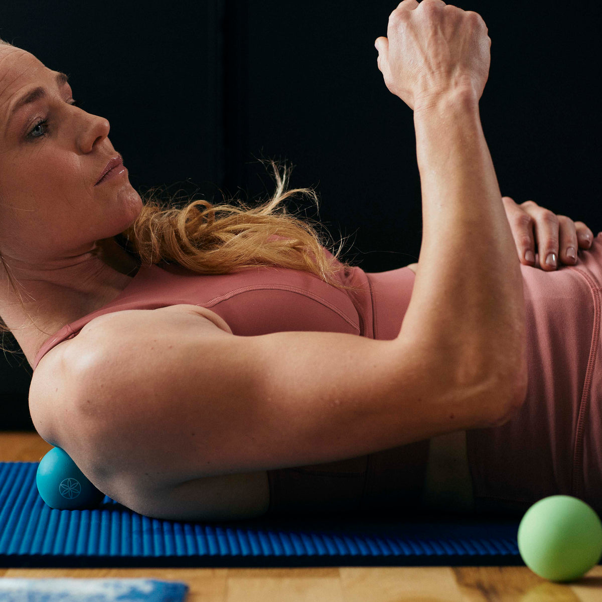 Person laying on a yoga mat with the Restore Pinpoint Massage Ball under the shoulder blade 