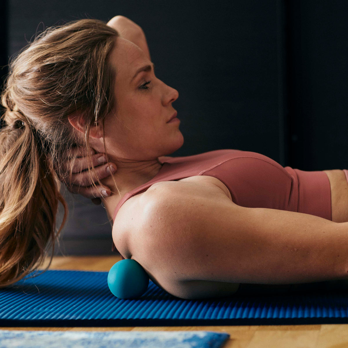 Person laying on yoga mat with Restore Pinpoint Massage Ball under the upper shoulder blade