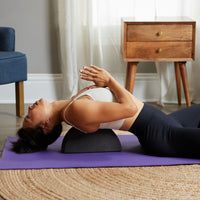 Person seated on floor, block under shoulders doing a back neck stretch 