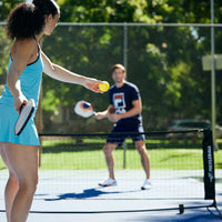 2 people playing Pickleball - 1 of them is getting ready to serve the ball over the net