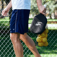Up close image of person outside carrying a Pickleball Paddle and a bag of 12 Pickleballs 