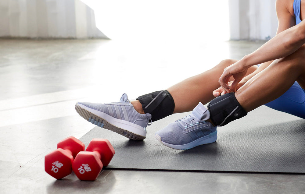 Red dumbbells on floor with person sitting with ankle weights on legs