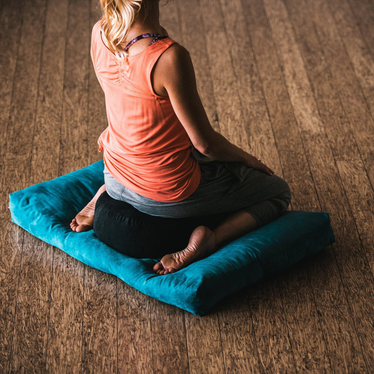 woman meditating on black zafu cushion on top of blue zabuton floor cushion