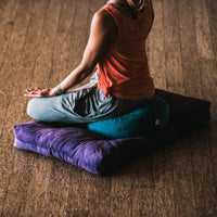View of Blue Zafu paired with the Purple Zabuton Cushion with Woman Meditating on them
