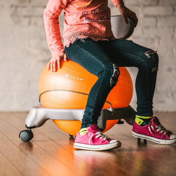 Sitting on the Kids Classic Balance Ball Chair in orange and grey